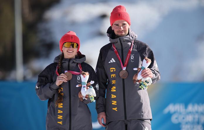 A female Para athlete and a male guide are posing for a photograph on the podium after receiving bronze medals